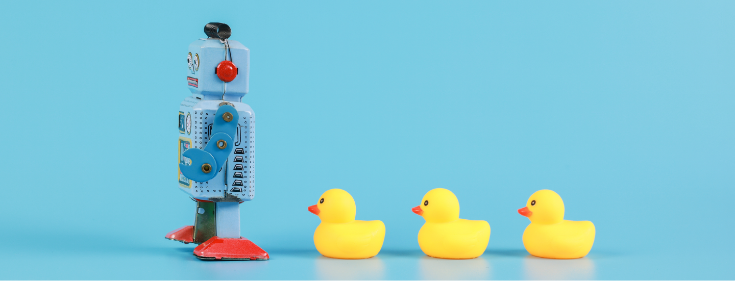 A metal toy windup robot leading a line of rubber ducks on a blue background