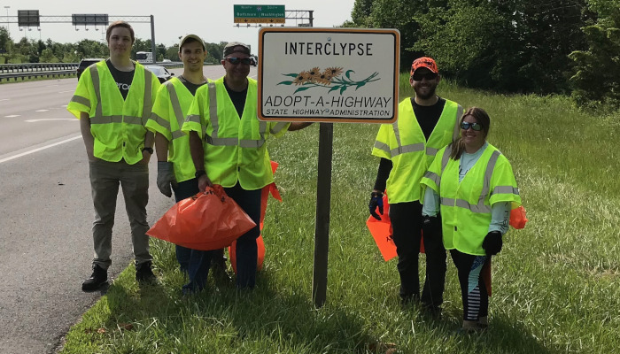 Interclypse employees posing next to their maryland adopt a highway sign